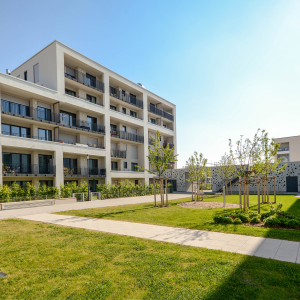 Contemporary mid-rise apartment building with balconies, landscaped courtyard, and young trees in a clean urban affordable housing development. 