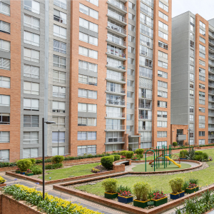 A landscaped courtyard with a small playground surrounded by mid-rise apartment buildings featuring brick and concrete facades. 